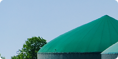Large green-roofed industrial tanks with trees and clear blue sky in the background.
