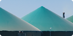 Three large, green, conical industrial storage tanks are shown against a clear sky, with a small structure and a person visible on one of the tanks.
