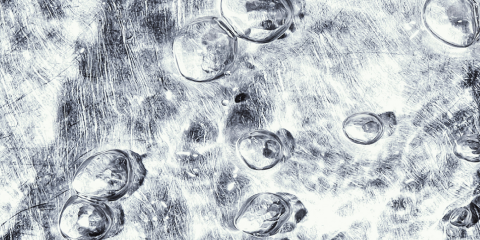 Close-up of bubbles suspended in a clear, textured sheet of ice, with visible scratches and patterns on the icy surface.
