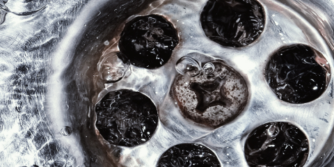 Close-up of a stainless steel sink drain with water flowing around and bubbles forming on the metal surface.