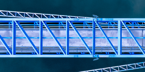 Aerial view of a blue metal bridge or structure spanning over a body of water, showing geometric lines and framework.