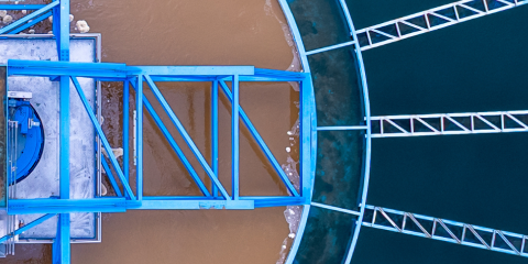 Aerial view of a water treatment facility showing a clear division between murky brown water and clean blue water, separated by blue structural beams.