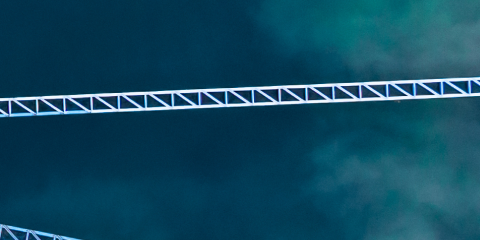 Aerial view of two white metal beams crossing over a body of deep blue-green water.